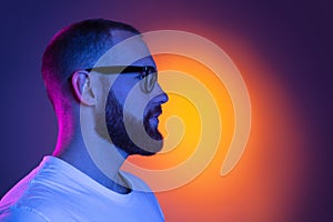 Close up portrait of young caucasian bearded man in sunglasses isolated on dark studio background in neon lights. Side