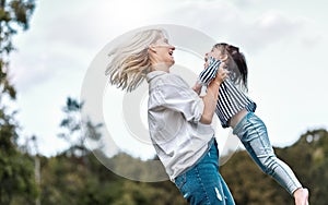 Side view image of happy little daughter playing with her smiling mother in the park. Loving woman and her little kid girl