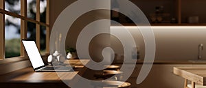 Side view image of a laptop on a hardwood desk against the window in a modern, cozy kitchen