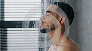 Side view indian relaxed man bearded guy naked male washes head hair face and beard in bathroom showering in at home in