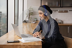 Side view Indian woman wearing headphones looking at laptop screen