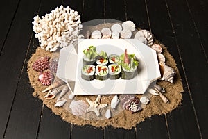 Side view of Japanese Veggie Futomaki Sushi Roll pieces with fresh vegetables on carton delivery takeaway box on dark wood