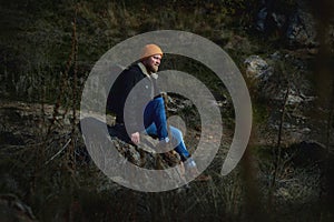 Side view of a lamber man in orange knitted woolen having rest on a rock in the steeppe after hiking and looking ahead. Plants in