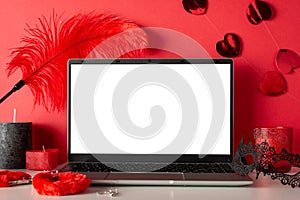 Side view of laptop, candles, mask, and adult toys furry handcuffs and feather tickler on red background