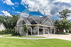 The side view of a large gray craftsman new construction house with a landscaped yard a three car garage and driveway