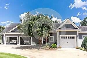 The side view of a large gray craftsman new construction house with a landscaped yard a three car garage and driveway