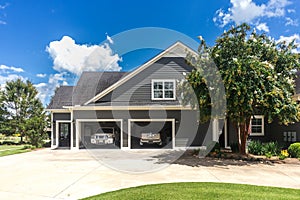 The side view of a large gray craftsman new construction house with a landscaped yard a three car garage and driveway