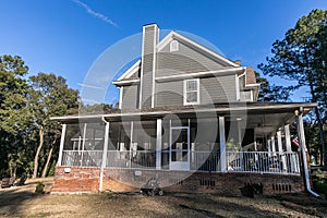 Side view of a large two story blue gray house with wood and vinyl siding with an expansive porch