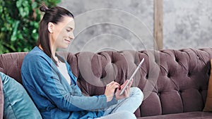 Side view laughing teenage young girl using tablet pc sitting on couch at cosiness living room