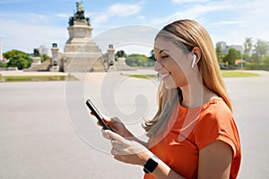 Side view of laughing young woman choosing the playlist watching her smartphone in Sao Paulo city park, Brazil