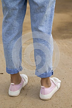 Side view of the legs of a teenage girl in pink sneakers and blue jeans against a background of yellow dry grass. The