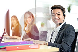 Side view of line of call centre employees are smiling and working on computers. Businesspeople In A Row Wearing Headset Working