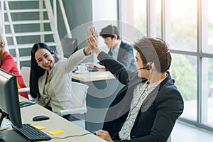 Side view of line of call centre employees are smiling and working on computers. Two of them are shaking hands