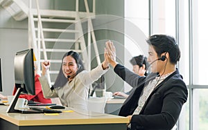 Side view of line of call center employees are smiling and working on computers. Two of them are shaking hands