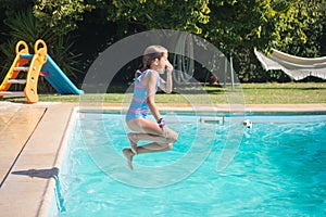 Side view of little Caucasian girl jumping into pool