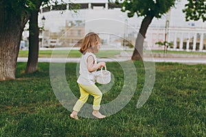 Side view of little cute child baby girl with basket running, play and have fun on green grass lawn in park. Mother