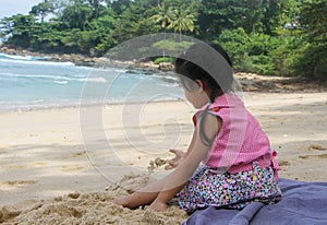 Side view of little cute girl dress casually sitting on the beach playing sand. Holiday, family, healthy child concept