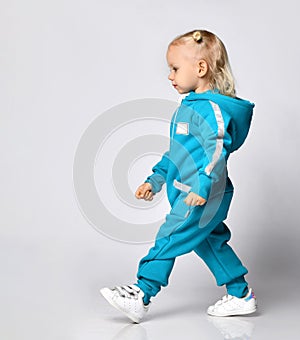 Side view of a little girl in a blue warm jumpsuit walking along the wall.