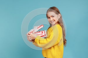Side view of little girl opens gift box, smiling to camera, celebrating birthday, Christmas holiday.