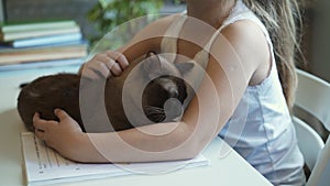 Side view of a little girl in white stroking her cat lying on the table