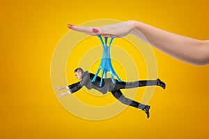 Side view of little man in suit hanging on blue sticky slime stuck to big woman`s hand above on yellow background. photo