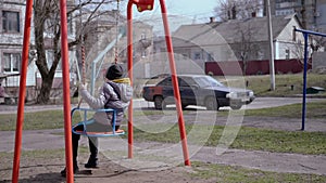 Side View, Lonely, Sad Child Swinging on a Swing in the Yard Without Friends