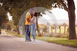 Side View Of Loving Couple Hugging As They Walk Along Track Through Countryside