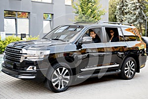 Side view of a luxury SUV vehicle with male driver and business lady