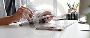 Male designer using digital tablet with stylus pen on white office desk with smartphone, computer device and other supplies