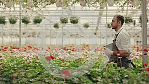 Side view of a male greenhouse worker walking holding the digital tablet. People, entrepreneurship and business concept.