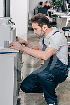 Side view of male handyman repairing copy machine photo