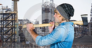 Side view of male hipster holding axe against factory