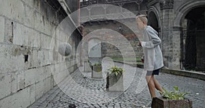 Side view of male kid soccer player kicking football ball with leg to wall . Young talented boy practicing tricks at old