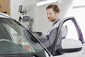 Side view of male maintenance engineer holding tablet PC while examining car in workshop