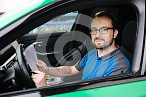 Side view on male mechanic fill document during car inspection. Man sits inside car and look into camera