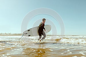 Side view of male surfer in wetsuit with his surfboard entering the sea. Surfing on ocean