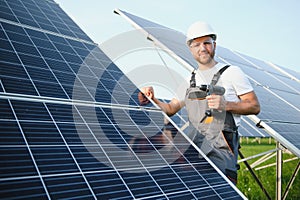 Side view of male worker installing solar modules and support structures of photovoltaic solar array. Electrician