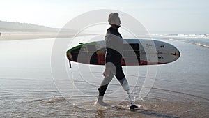 Side view of man with bionic leg going to ocean for surfing