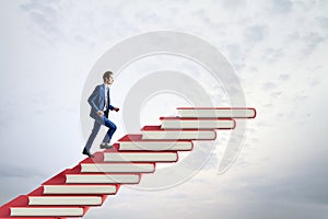 Side view of man climbing red book steps. Cloudy sky background with mock up place. Growth and education concept