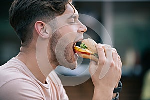side view of man eating tasty burger