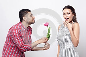 Side view man giving tulip to excited woman. Portrait of handsome man in red checkered shirt and beautiful woman in white striped