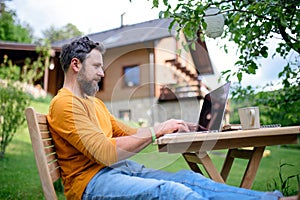 Side view of man with laptop working outdoors in garden, home office concept.