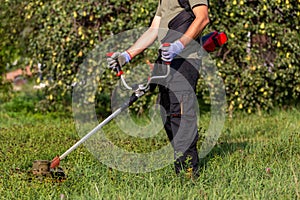 Side view of man mowing the grass at his garden by using string trimmer