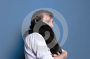 Side view of man in shirt holding black cute cat on sholder