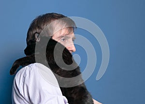 Man in shirt and holding and holding black cute cat on sholder on blue background photo