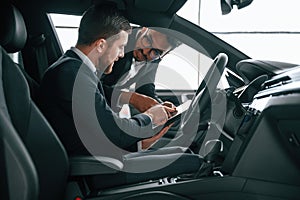 Side view. Man showing automobile interior to the customer