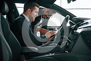 Side view. Man showing automobile interior to the customer