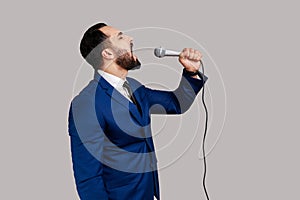 Side view of man singing songs, holding microphone, singer making performance, keeps eyes closed.