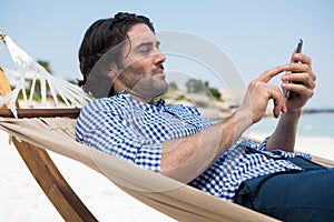 Side view of man using mobile while relaxing in hammock