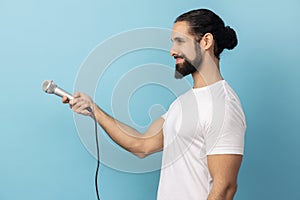 Side view of man wearing white T-shirt holding microphone, making interview and asking opinion.